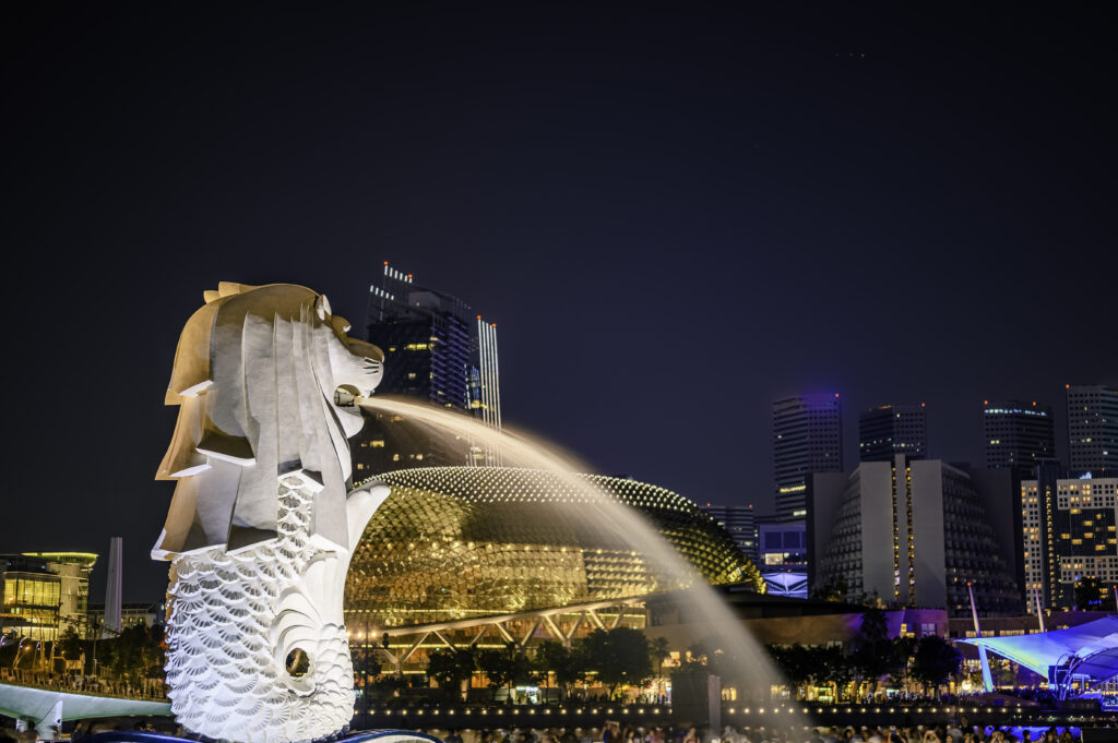 Merlion Statue Fountain In Merlion Park And Singapore City Skyline At Night.